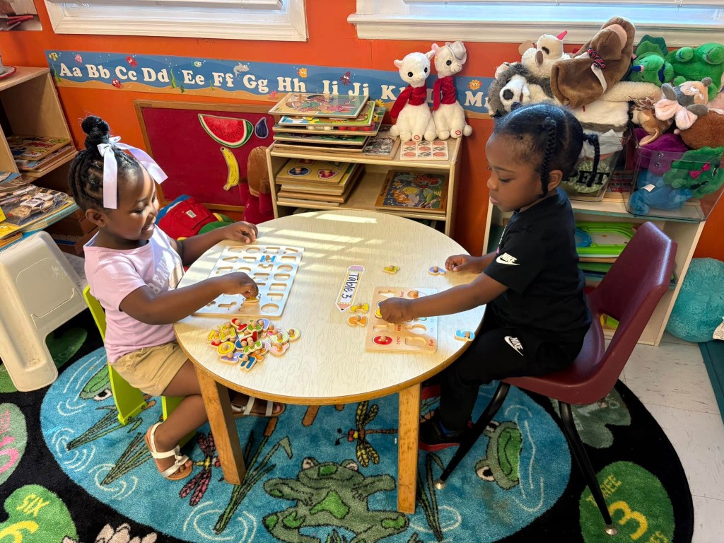 Two preschoolers doing alphabet and number puzzles together at a table