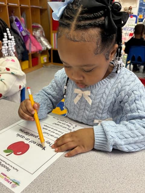 Preschooler working on a reading worksheet with an apple theme in the classroom
