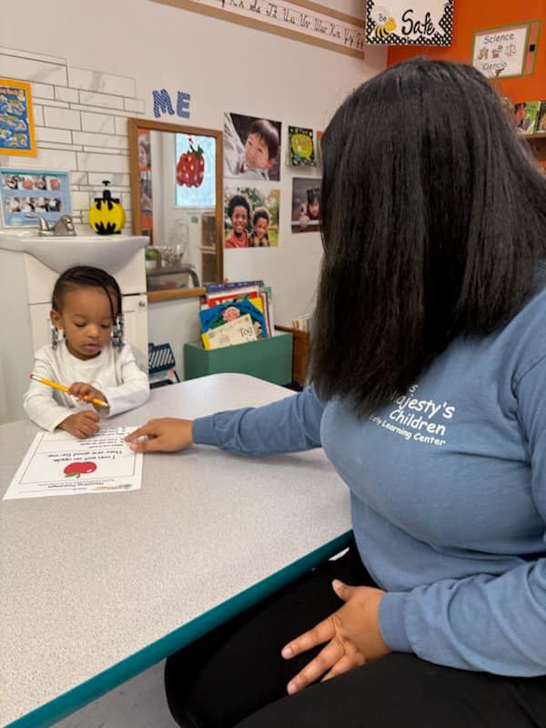 Teacher in His Majesty's Children shirt helping a student one-on-one with a learning activity